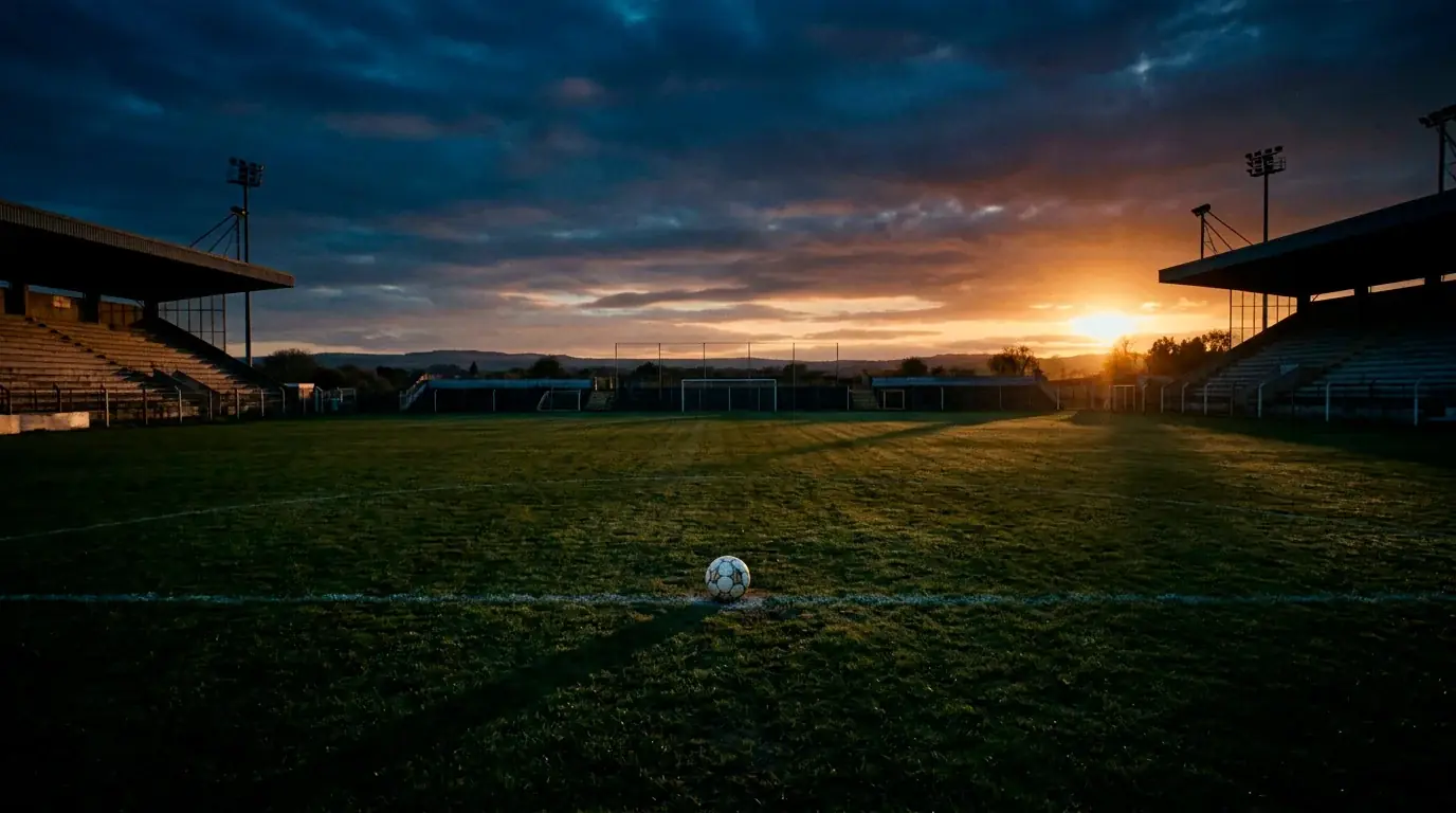 An empty soccer pitch at dusk with a ball on the centre spot and long shadows, symbolic underdog mood